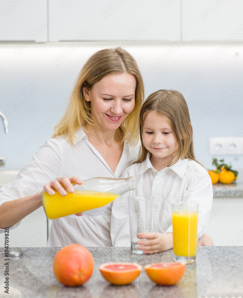mother and baby daughter drinking orange juice in the kitchen mother and baby daughter drinking orange juice in the kitchen