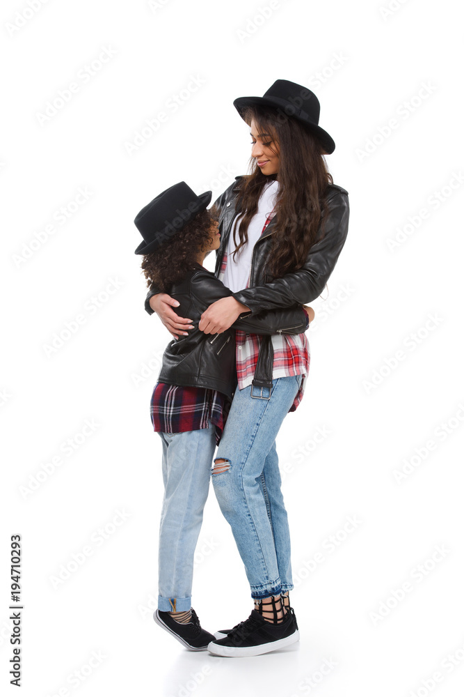 stylish happy mother and daughter in leather jackets embracing and looking at camera isolated on white stylish happy mother and daughter in leather jackets embracing and looking at camera isolated on white