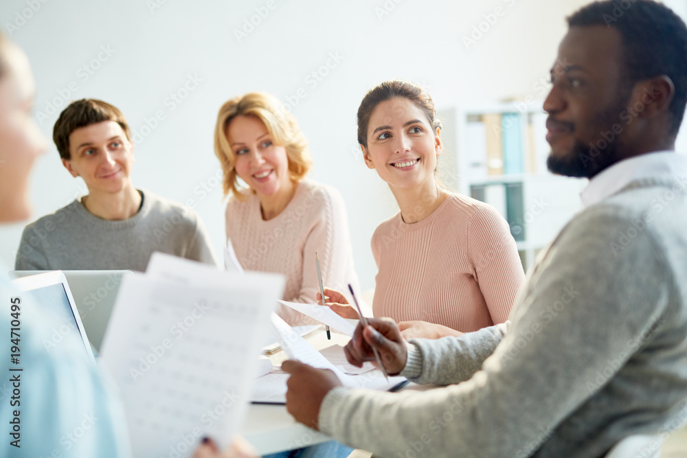 Happy young businesswoman looking at one of colleagues with smile while listening to his explanation Happy young businesswoman looking at one of colleagues with smile while listening to his explanation