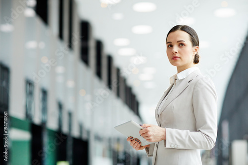 Pensive businesswoman in elegant formalwear browsing in the net on the move