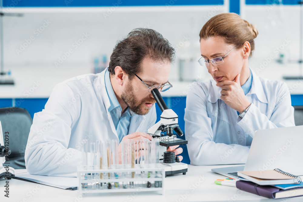 portrait of scientific researchers in white coats working together at workplace with microscope in laboratory portrait of scientific researchers in white coats working together at workplace with microscope in laboratory
