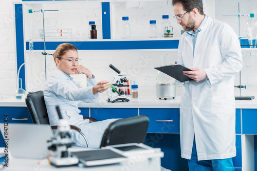 scientific researcher looking at flask with reagent in hand with colleague near by in laboratory