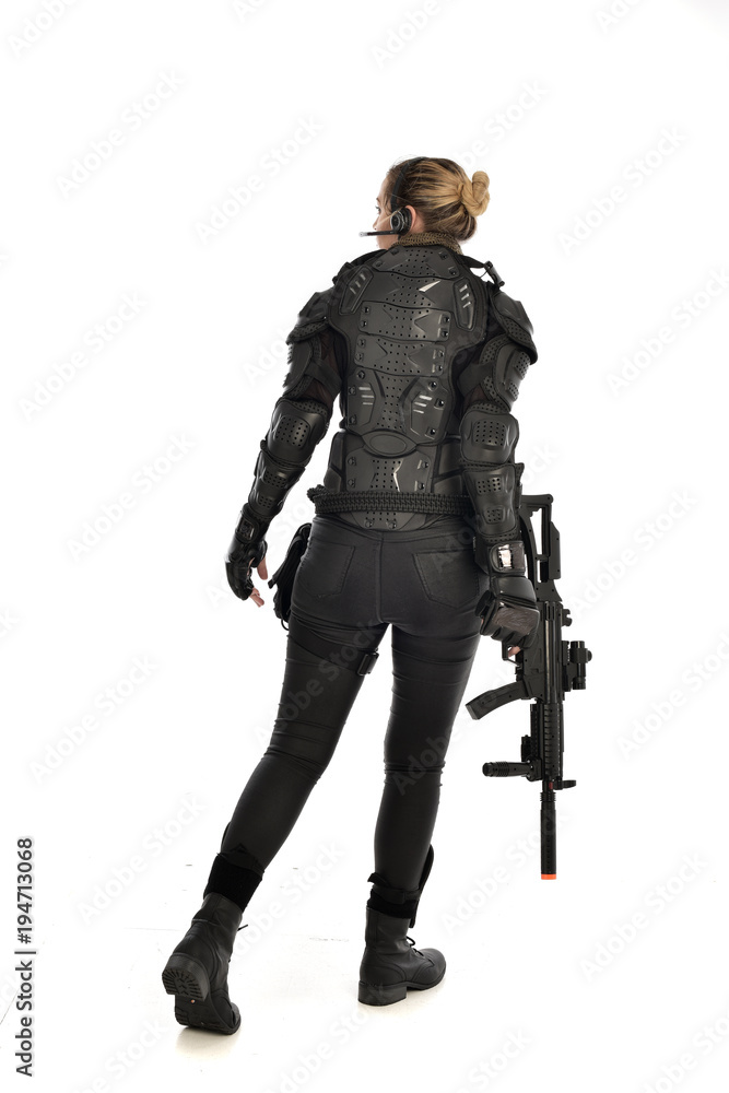 full length portrait of female soldier wearing black tactical armour, standing with back to the camera holding a gun, isolated on white studio background. full length portrait of female soldier wearing black tactical armour, standing with back to the camera holding a gun, isolated on white studio background.