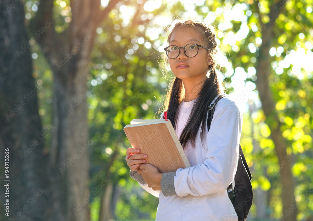 Asian female student embracing a book standing in the garden,Summer study concepts. Asian female student embracing a book standing in the garden,Summer study concepts.