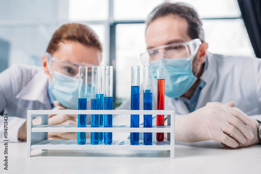 selective focus of scientific researchers in googles and medical masks looking at reagents in tubes in lab selective focus of scientific researchers in googles and medical masks looking at reagents in tubes in lab