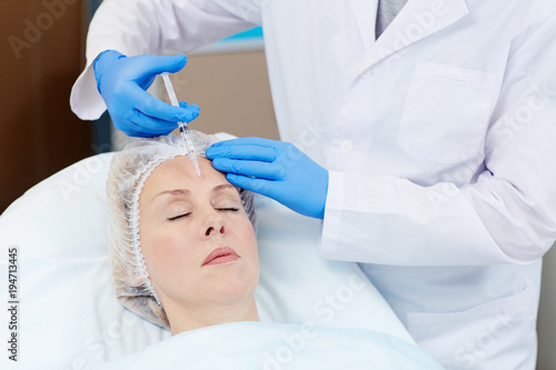 Close up of hands of expert beautician injecting botox in female forehead