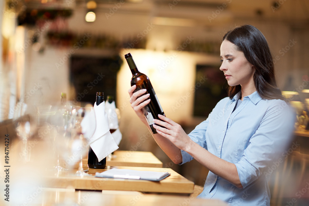 Female sommelier holding a bottle of wine and reading information on it