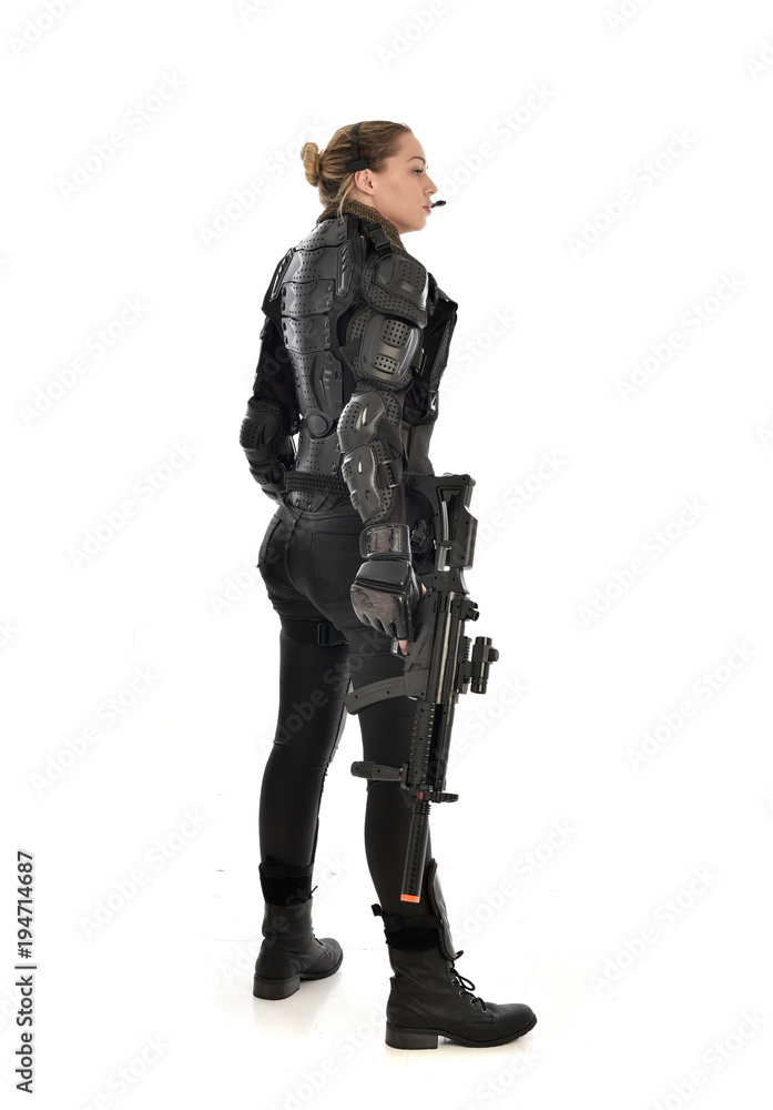 Fototapeta premium full length portrait of female soldier wearing black tactical armour, standing with back to the camera holding a gun, isolated on white studio background.
