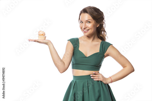 Brunette pretty beautiful caucasian woman in green festive dress showing proposing holding sweet cupcake dessert in her palms. Isolated white background