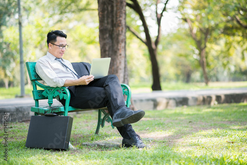 Businessman sitting on the park bench with laptop