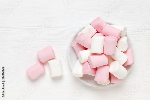 White and pink marshmallow on a saucer on a white wooden surface