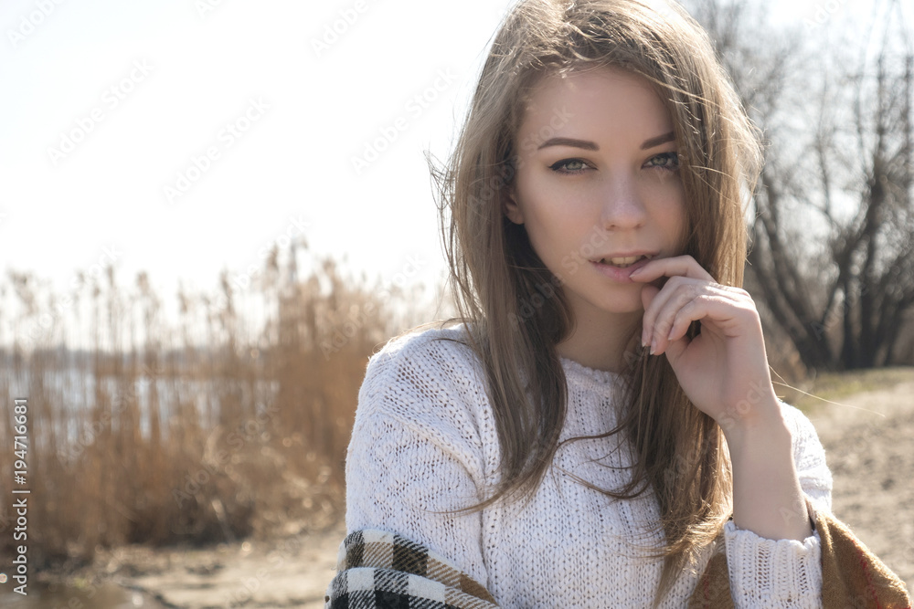 Beautiful young teenage caucasian woman in a plaid walking thinking a bit sad in a park near river (lake) in spring (autumn) cold windy weather. lifestyle portrait in nature. Copy space Beautiful young teenage caucasian woman in a plaid walking thinking a bit sad in a park near river (lake) in spring (autumn) cold windy weather. lifestyle portrait in nature. Copy space