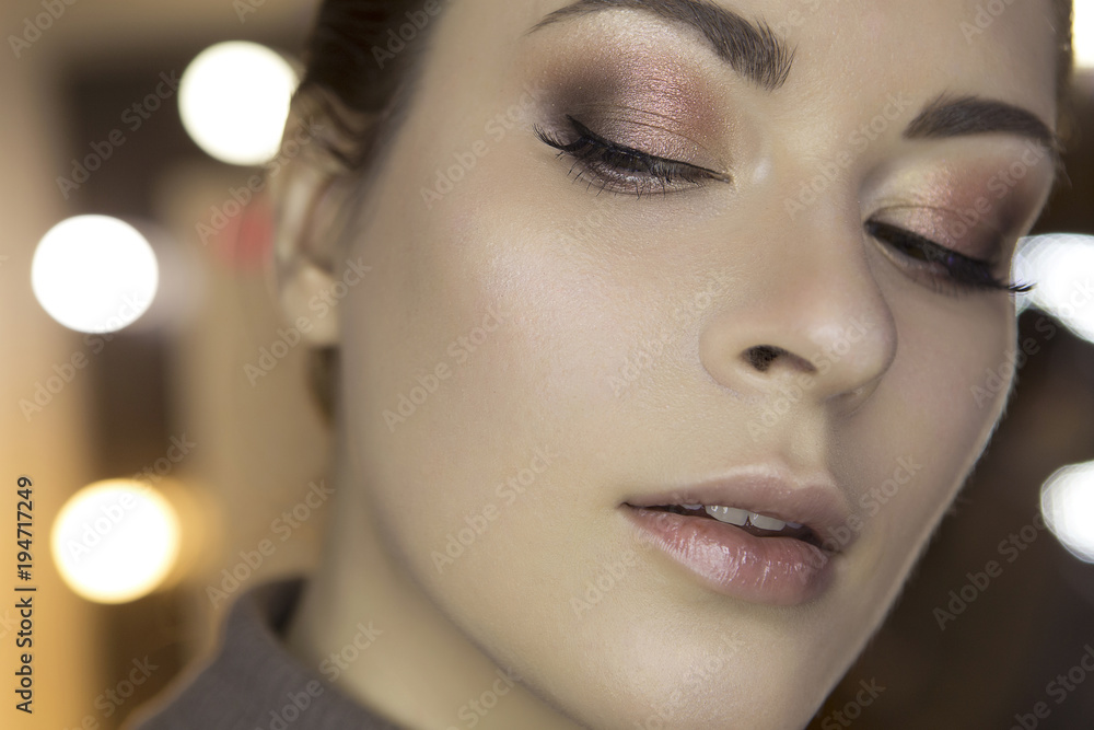 Cute beautiful young caucasian brunette woman with evening make up in casual outfit posing with neutral emotions. Mirror with lights on a background. Close up of a fresh clean face skin. Copy space Cute beautiful young caucasian brunette woman with evening make up in casual outfit posing with neutral emotions. Mirror with lights on a background. Close up of a fresh clean face skin. Copy space