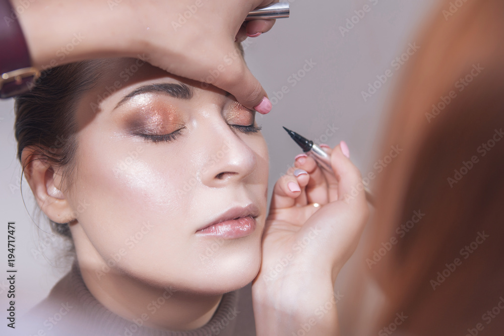 Professional make up artist apply mascara to a young caucasian woman on her date and wedding photosession. Indoors, studio. Casual outfit. Backstage of a process