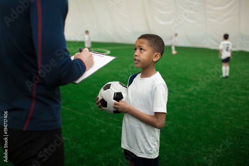 Adorable football player with ball talking to his trainer on pitch after game © pressmaster