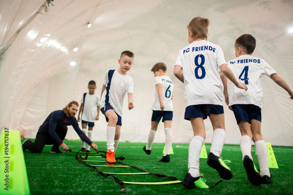 Fototapeta premium Football team of adorable boys exercising on green pitch on special facilities