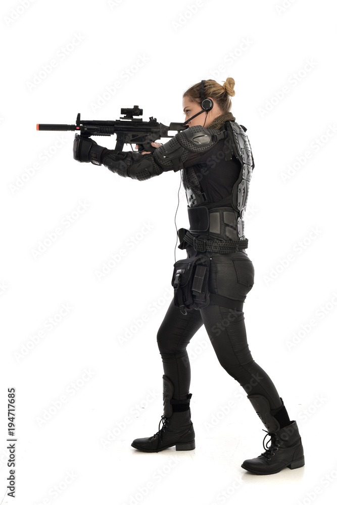 full length portrait of female soldier wearing black tactical armour, standing with back to the camera holding a gun, isolated on white studio background. full length portrait of female soldier wearing black tactical armour, standing with back to the camera holding a gun, isolated on white studio background.