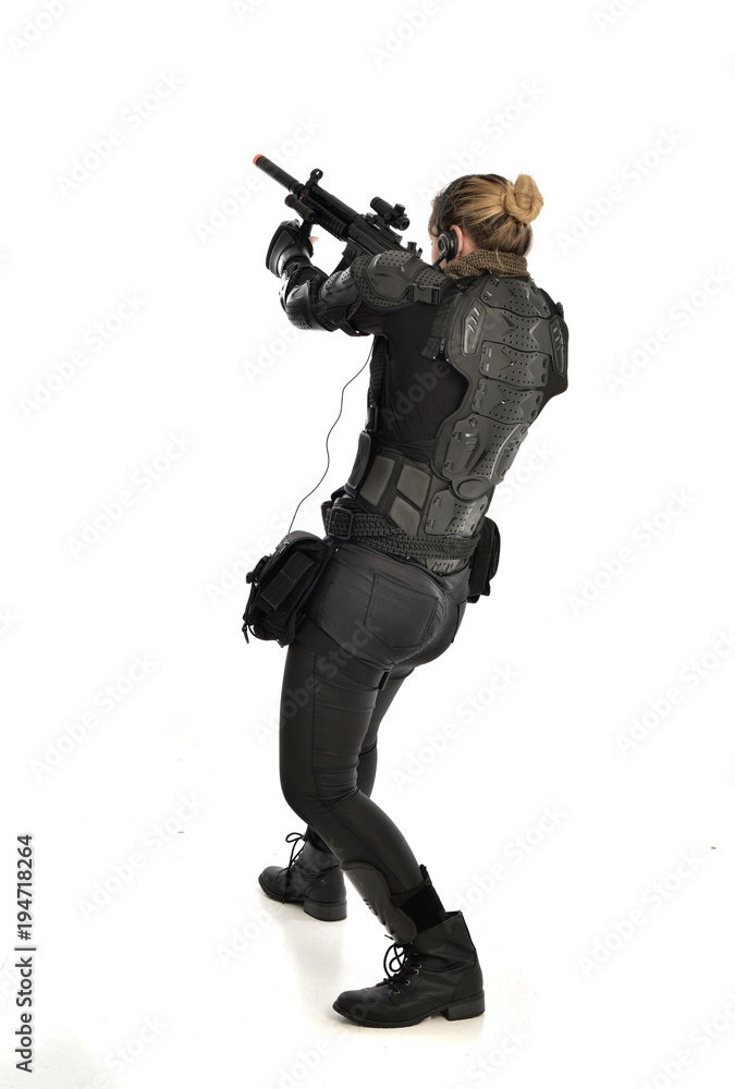 full length portrait of female soldier wearing black tactical armour, standing with back to the camera holding a gun, isolated on white studio background. full length portrait of female soldier wearing black tactical armour, standing with back to the camera holding a gun, isolated on white studio background.