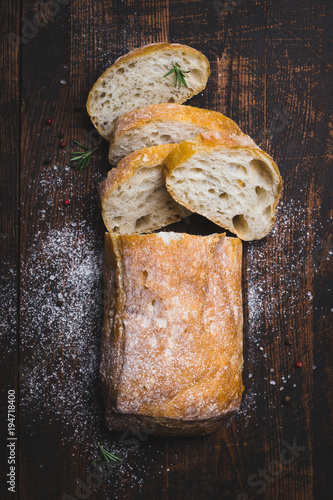 Italian ciabatta bread cut in slices on dark wooden background photo