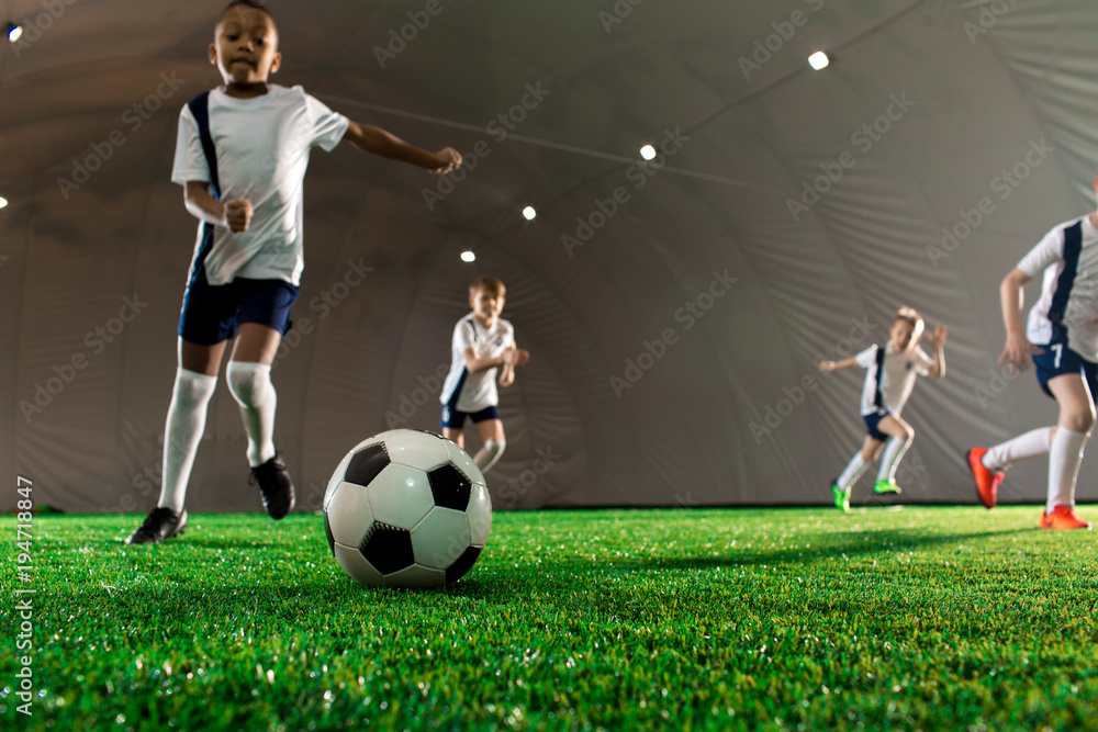 Soccer ball on green pitch and little players running towards it during game