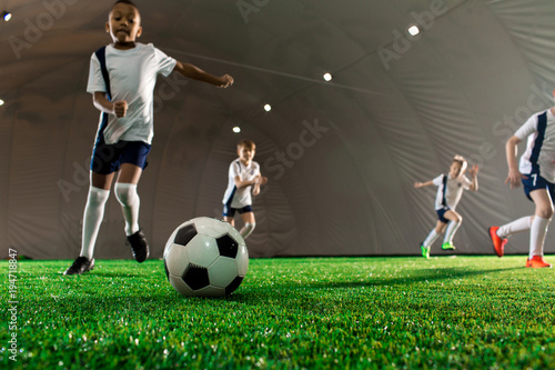 Soccer ball on green pitch and little players running towards it during game © pressmaster