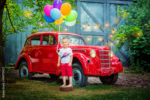 Happy little child holding balloons on background of red retro car in park