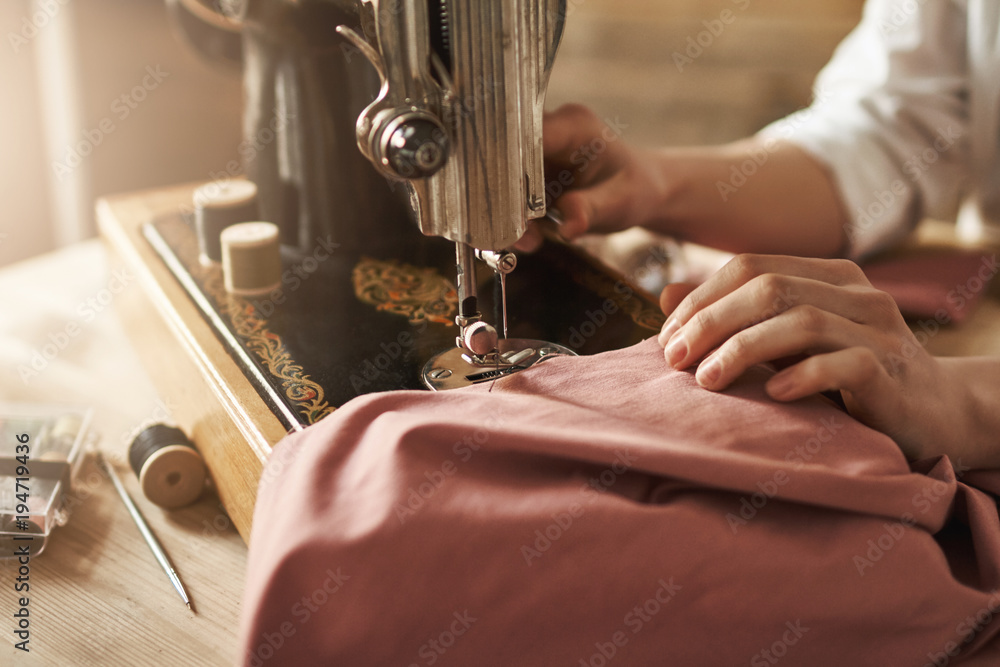 Sewing keeps my mind relaxed. Cropped shot of female tailor working on new project, making clothes with sewing machine in workshop, being busy. Young designer making her ideas come true - obrazy, fototapety, plakaty 