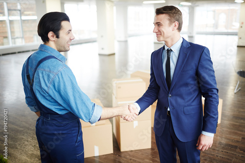 Young businessman in suit and delivery man in uniform handshaking after relocation work