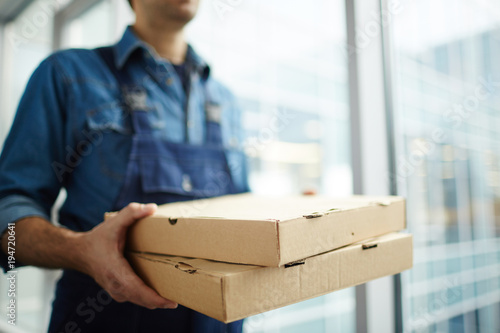 Two boxes with fast food being carried by delivery man in uniform for one of clients photo