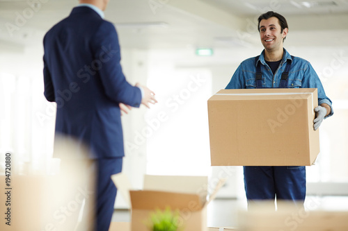Young courier carrying big box to office worker while helping him to relocate