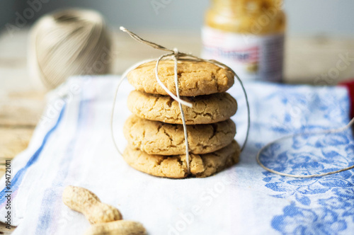 Freshly baked homemade peanut butter cookies.A stack of cookies tied with a string. Peanuts on a side.