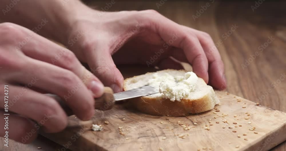 man hands spreading cream cheese on baguette slice on wood board