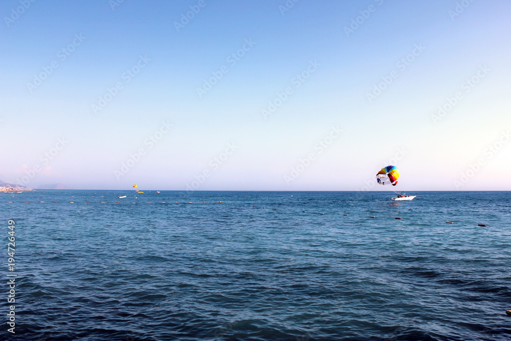 Blue Mediterranean sea.  People fly by parachute in the blue sky over the sea in clear weather, a holiday at sea, parachute flying over the sea, towing by a boat