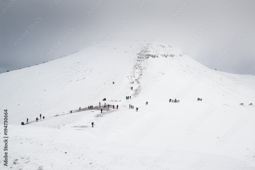 Cloud covered winter landscape of Corn Du mountain in Brecon Beacons with people hiking to the summit