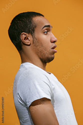 Doubtful Afro-American man is looking frightenedly against orange background photo