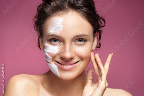 Young woman with moisturizing facial mask on pink background. Photo of pretty woman receives the spa treatments. Beauty   Skin care concept