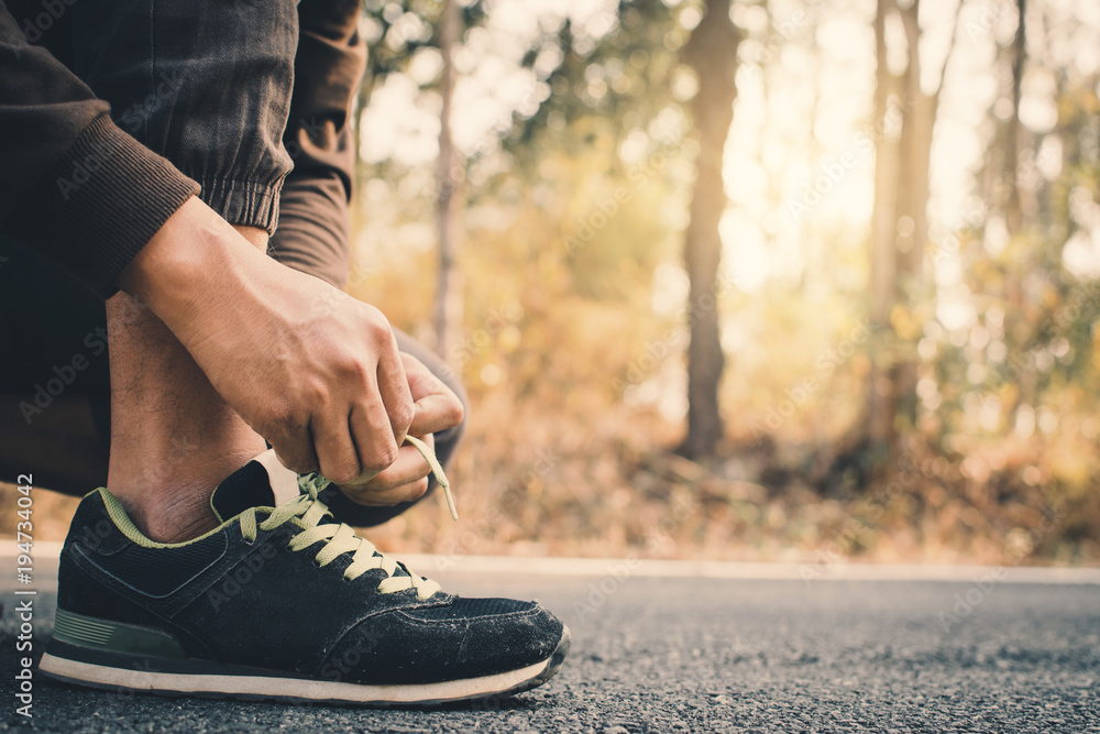 Close-up hands of man tying shoelace during running on the road for health, color of vintage tone selective and soft focus