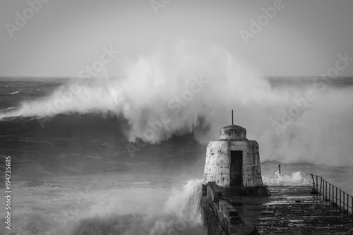 Large wave breaks off Portreath harbor wall - black and white
