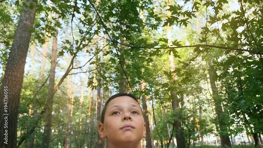 A zoom out view of a thoughtful nine year boy standing in a picturesque park in summer in slow motion. He looks up being charmed A zoom out view of a thoughtful nine year boy standing in a picturesque park in summer in slow motion. He looks up being charmed