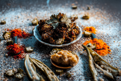 Popular Indian Brunch dish i.e Barali bindi/crispy okra or bharli bindi a dish made from raw ladies finger and other vegetables with spices by frying it.On a wooden surface in dark Gothic colors. photo