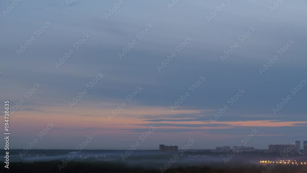 Distant high-rise apartment blocks in the dusk. Scene with evening sky and fog drifting over the trees