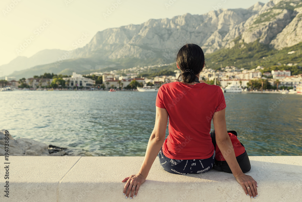 Fototapeta premium Girl sitting on a pier and watching the sunset.