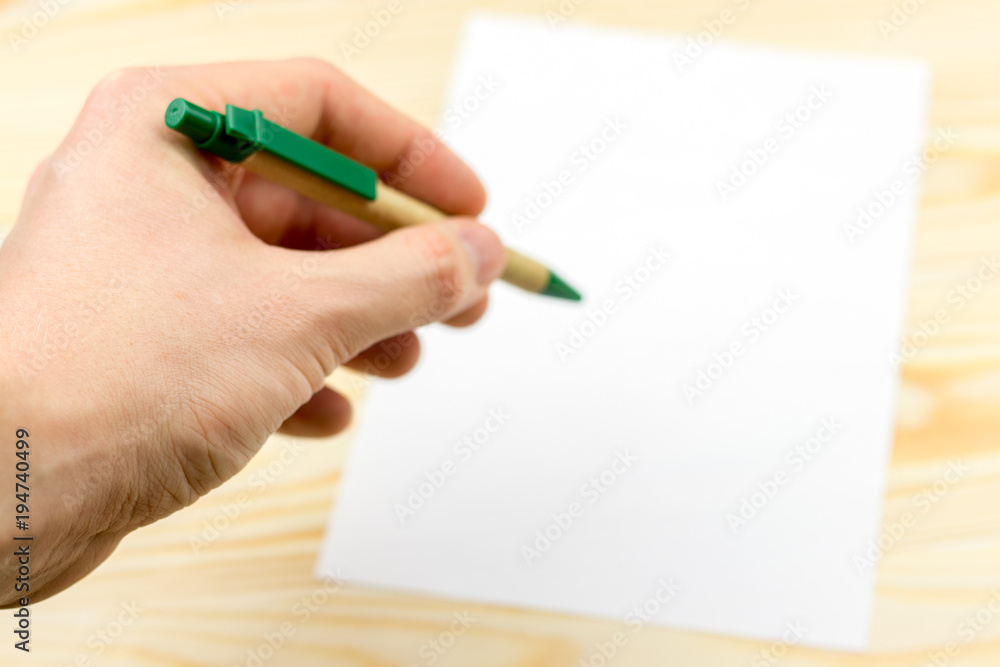 Hand holds pen on wooden background with sheet of white paper Hand holds pen on wooden background with sheet of white paper
