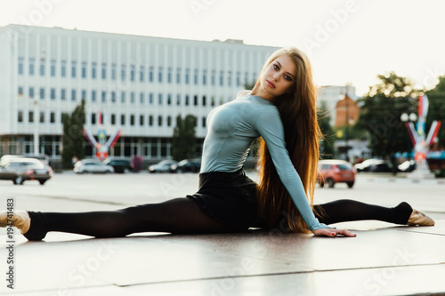Ballerina sitting in gymnastic pose in middle of city street. buildings background.