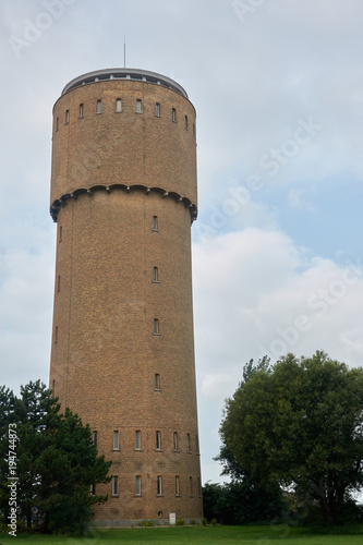 Water tower made of red brick with narrow windows next to trees