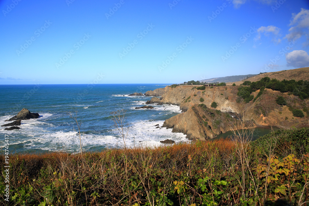 Peaceful setting along waterfront park in Monterey, California with benches, paths, and ocean beach.