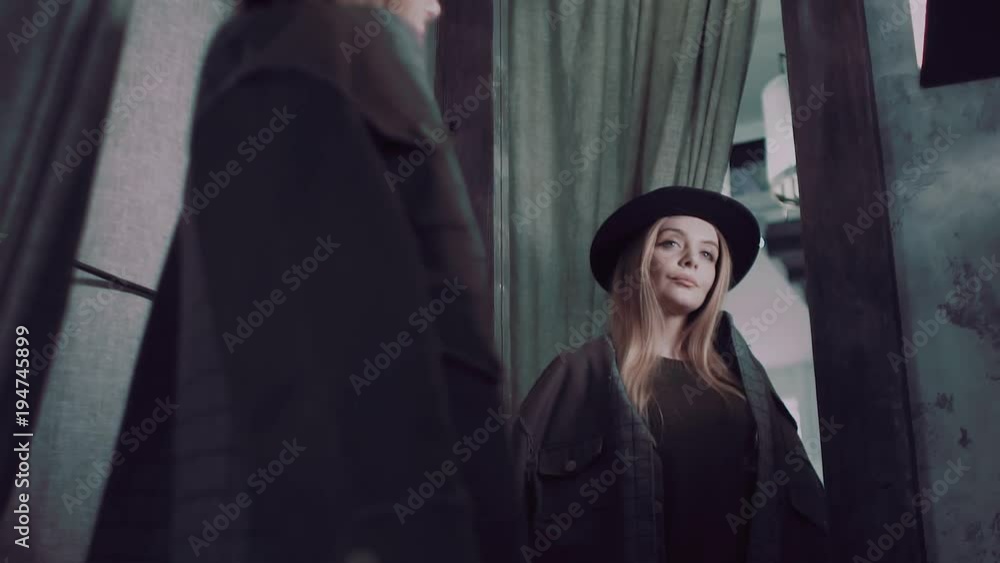 Stylish girl in a changing room, looking at herself in a mirror measuring her coat Stylish girl in a changing room, looking at herself in a mirror measuring her coat