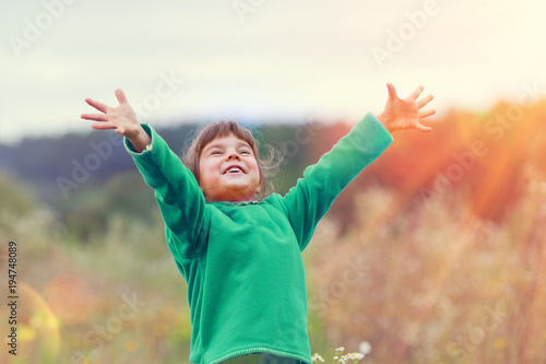 Happy laughing little girl with hands in the air walking in the field