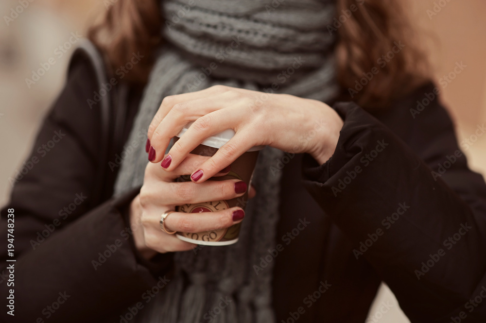 Young girl in warm scarf on the street holding coffee to go or take away while walking in the park, mock-up of coffee cup