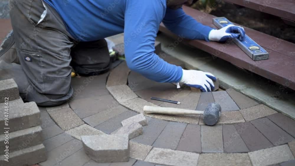 Man putting bricks in place for a decorative two tone paver pattern in front a stairway. Man putting bricks in place for a decorative two tone paver pattern in front a stairway.